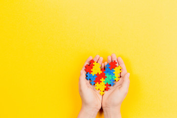Child hand holding colorful heart on yellow background. World autism awareness day concept