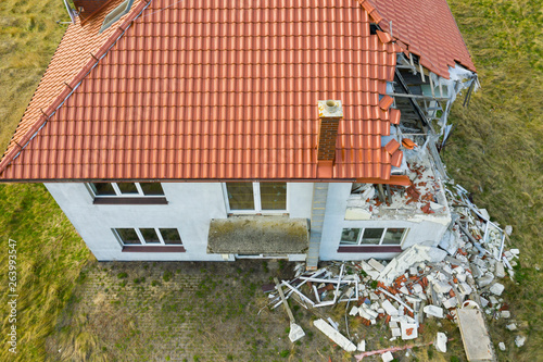 Aerial view on damaged red single house roof after strong wind or explosion. Hole in the rooftop and floor. Rubble on the ground