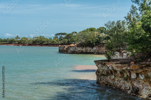 Darwin Australia - February 22, 2019: Semi Long view on East Point Shoreline shows brown, yellow and darker rocky cliffs covered by green vegetation under blue sky and greenish sea water of Beagle Gul