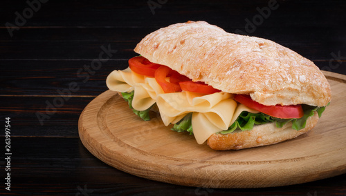 Ciabatta sandwich with lettuce , prosciutto and cheese on wooden board with copy space