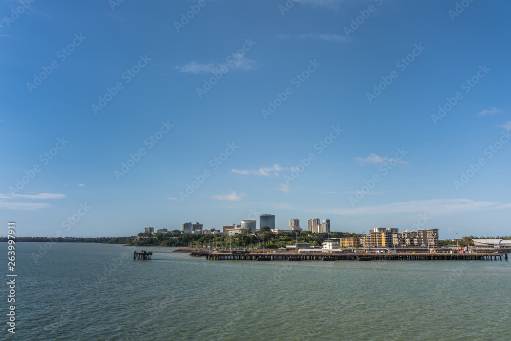 Darwin Australia - February 22, 2019: western side of Darwin skyline seen from south upon harbour bay water under blue sky. Convention center to the left. Dock for larger ships up front. 