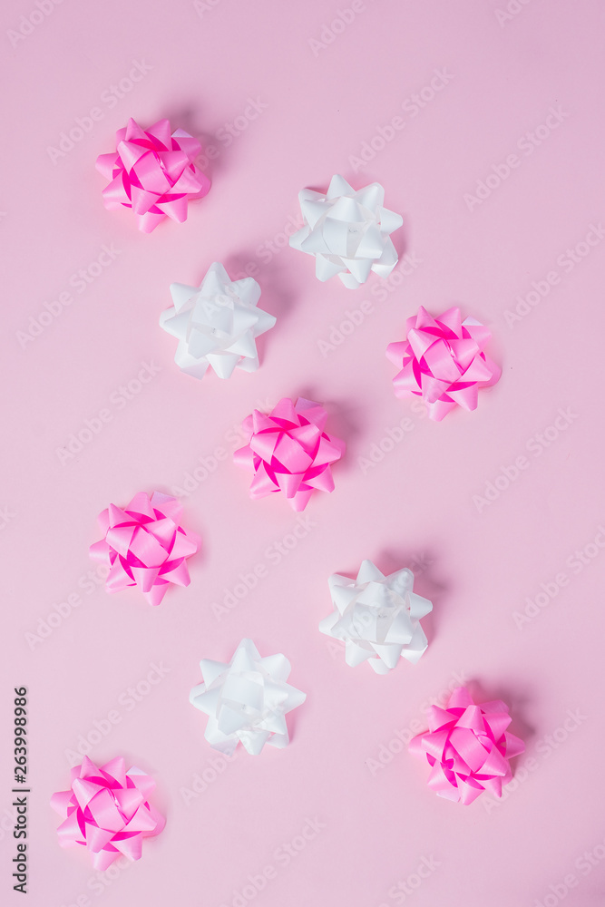 Pink and white ribbon bow on pink background. Greeting card with copy space. Vertical image.Holiday decorations. Creative flat lay.
