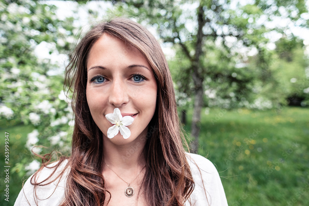 Portrait of smiling young woman with apple blossom in her mouth Portrait of smiling young woman with apple blossom in her mouth