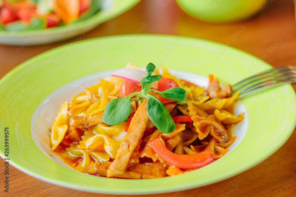 Farfalle pasta with the chicken and tomatoes on a green plate.