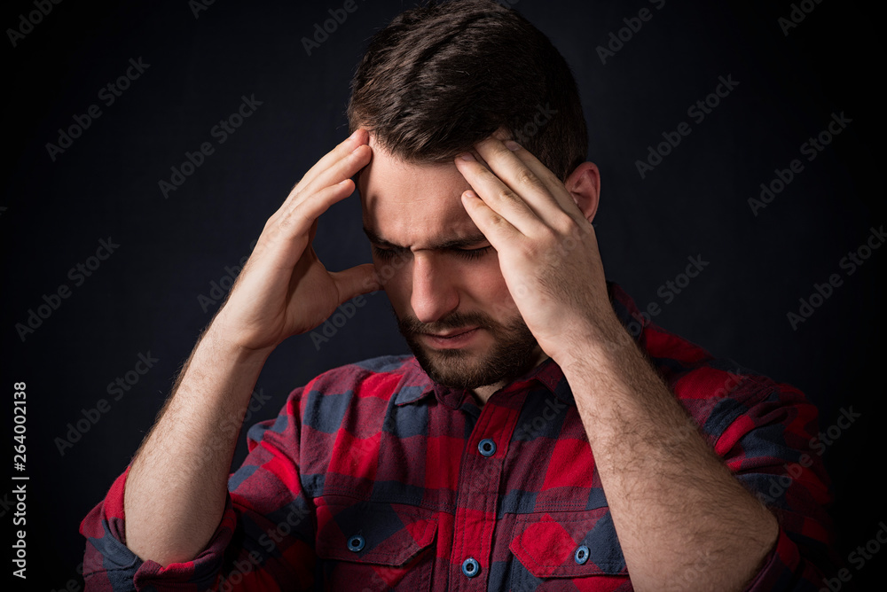 young man in plaid shirt suffers from headache against black background young man in plaid shirt suffers from headache against black background