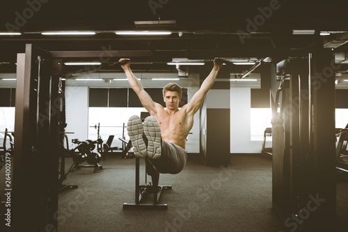 Obraz na plátně Shirtless muscular handsome young man doing exercises on horizontal bar in a gym club