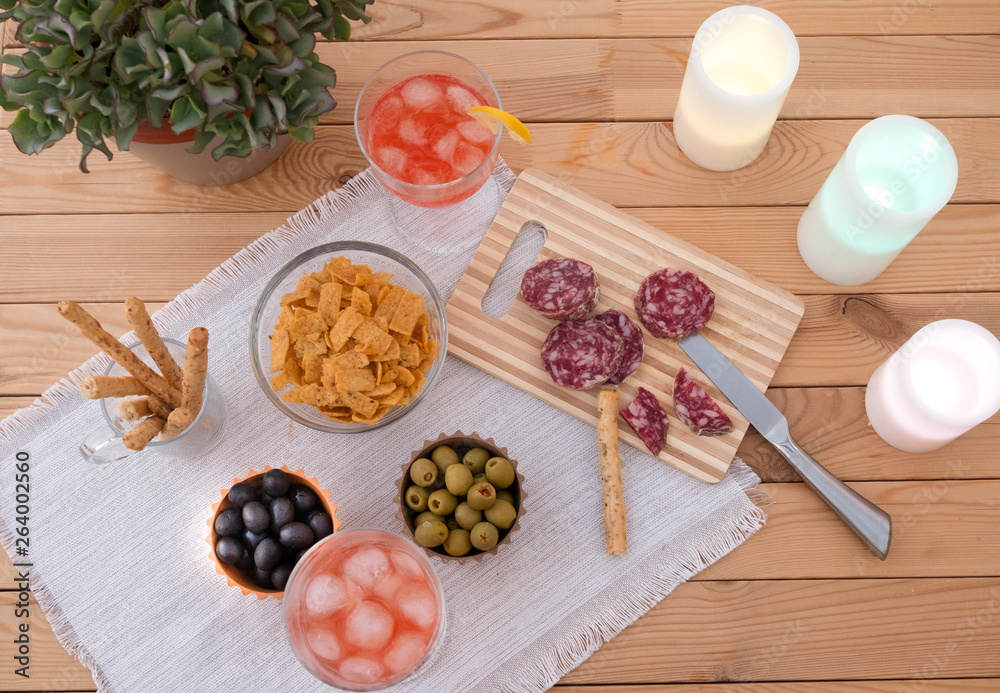 Enjoying a relaxed moment. Aerial view of a wooden table with some snack as salami olives green and black and two red wineglass.