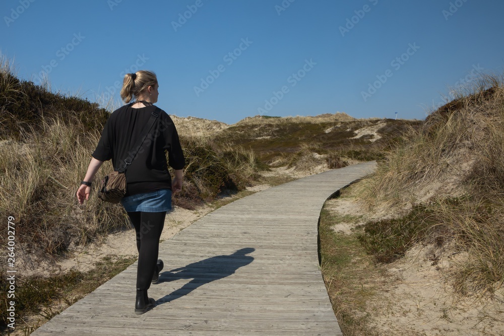 Frau geht auf einem schönen Pfad durch malerische Dünen Landschaft auf Sylt