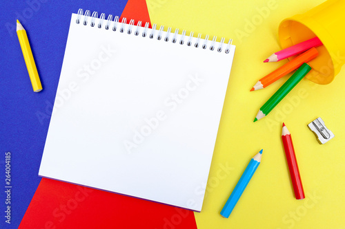 Blank notepad, color pencils and a sharpener on a color paper background. Drawing tools. Kid’s leisure and education materials.
