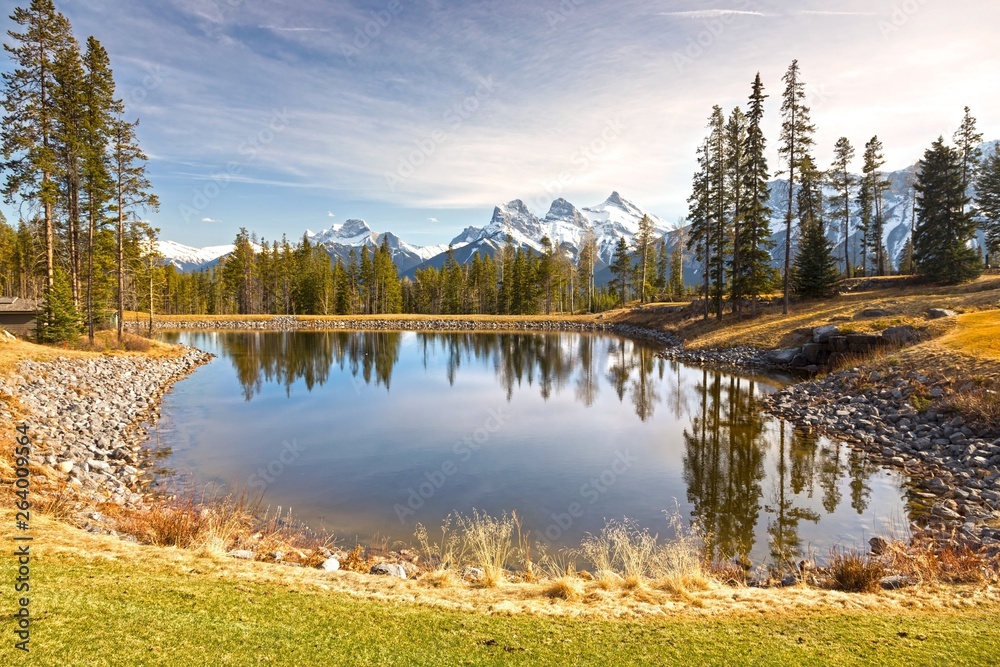 Scenic Springtime Landscape View of Distant Snowcapped Mountain Peaks, Green Grassland and Blue Lake above City of Canmore in Alberta Foothills of Canadian Rockies near Banff National Park