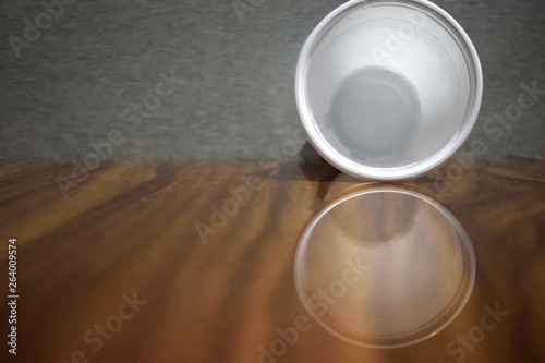 empty  plastic cup standing on wooden table  with reflection and grey background 