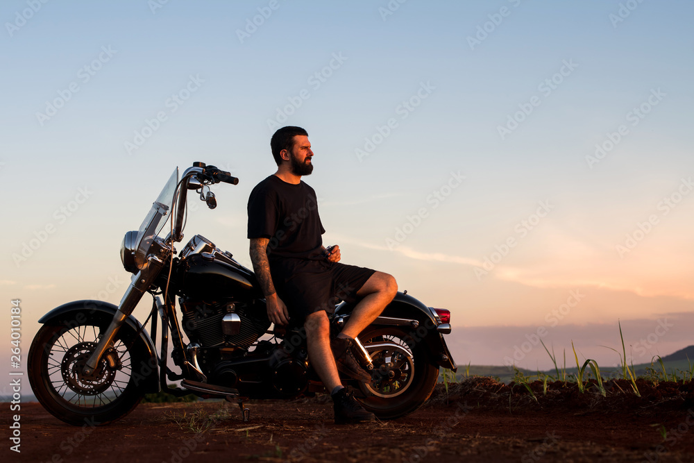 Young man sitting on his custom classic motorcycle admiring the landscape