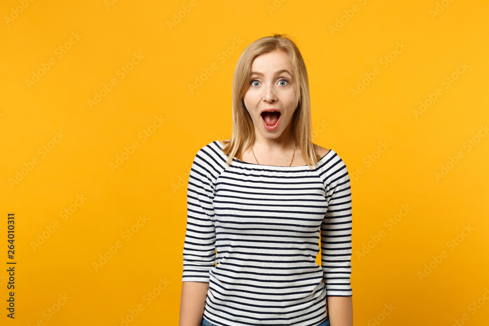 Beautiful shocked young blonde woman in striped clothes looking camera isolated on bright yellow orange wall background, studio portrait. People sincere emotions lifestyle concept. Mock up copy space. Beautiful shocked young blonde woman in striped clothes looking camera isolated on bright yellow orange wall background, studio portrait. People sincere emotions lifestyle concept. Mock up copy space.