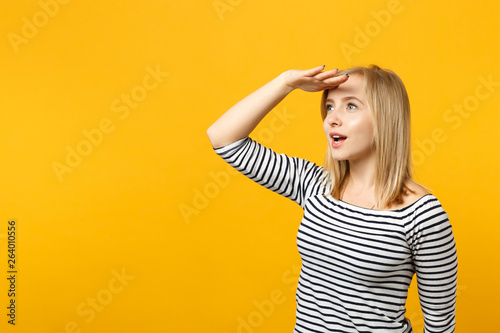 Amazed young woman in striped clothes holding hand at forehead looking aside far away†distance isolated on yellow orange wall background. People sincere emotions lifestyle concept. Mock up copy space.