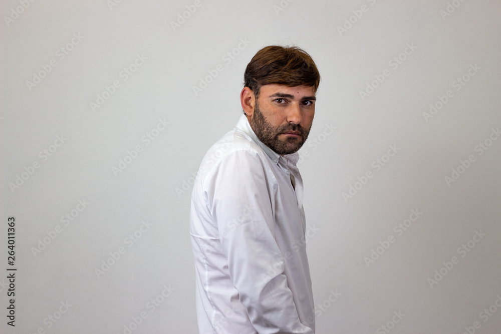 Fashion portrait of handsome young man with brown hair looking ashamed, their back facing the camera and looking at the camera. Isolated on white background.