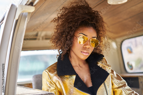 stylish edgy african american woman wearing golden jacket and sunglasses in old van photo
