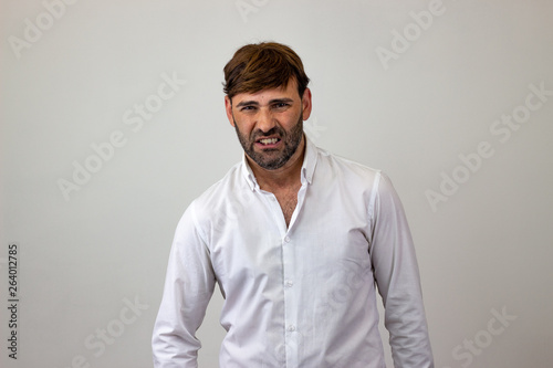 Fashion portrait of handsome young man with brown hair looking disgusted, looking at the camera. Isolated on white background.