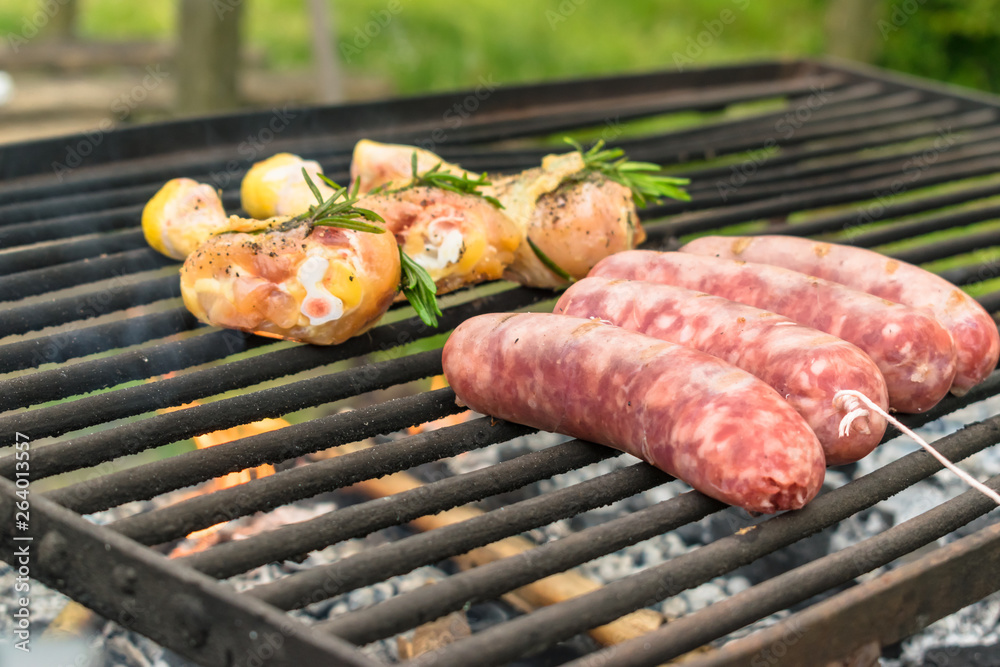 Tasty meat being barbecued on a rustic embers grill in a garden. Chicken with herbs and sausages.
