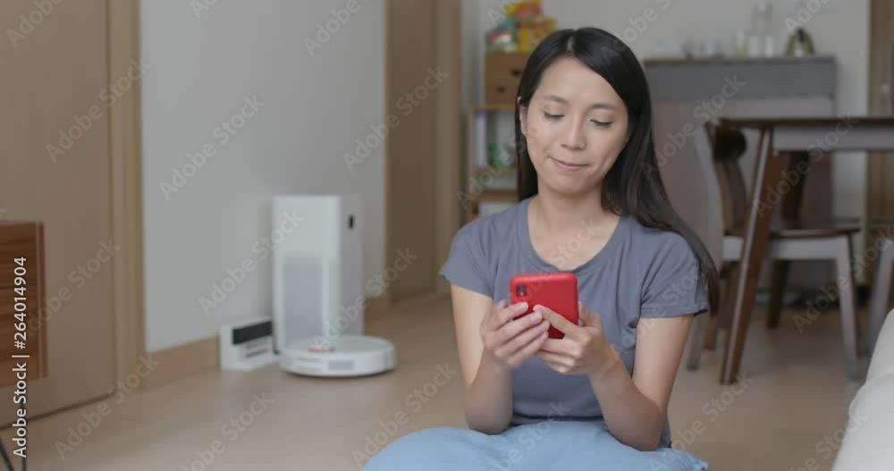 Woman use of mobile phone to control robotic vacuum cleaner at home Woman use of mobile phone to control robotic vacuum cleaner at home