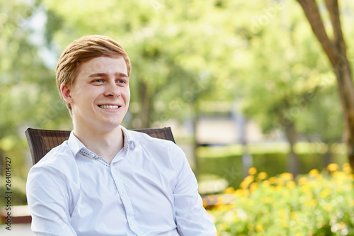 Young attractive man in white shirt sitting on brown chair in the park on green background