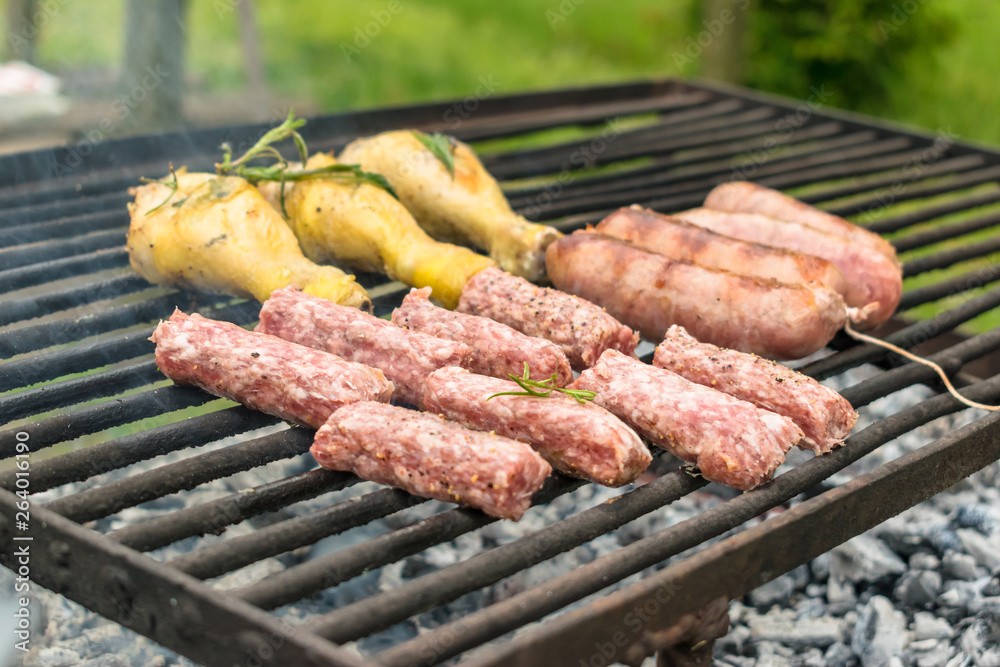 Tasty meat being barbecued on a rustic embers grill in a garden. Chicken with herbs and sausages.