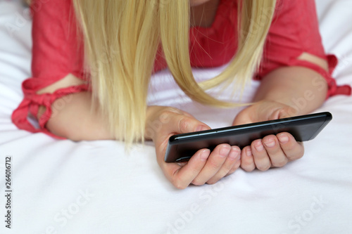 Blonde woman watching video on smartphone, sexy girl lying on the bed with mobile phone. Concept of online addiction, home leisure, porn movies, video chat