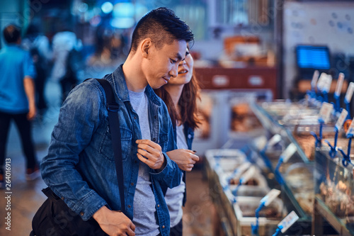 Young asian couple looking for something special at traditional chainese market. They are pensive. A lot of seafood at background. photo