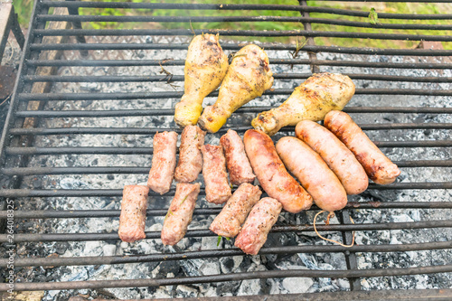 Tasty meat being barbecued on a rustic embers grill in a garden. Chicken with herbs and sausages.
