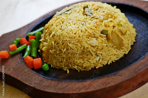 Closeup photo of traditional indian curry rice with vegetables on wooden plate.