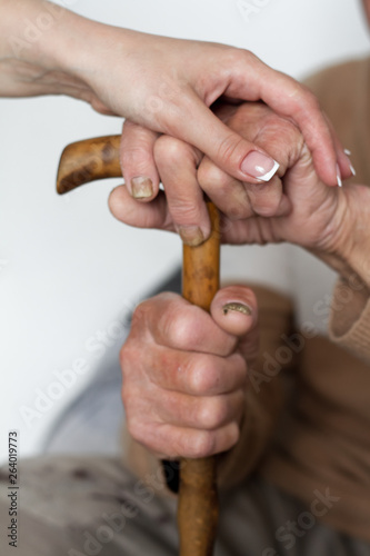 Closeup of senior mans hands and young girl caregiver holding hands on walking stick.