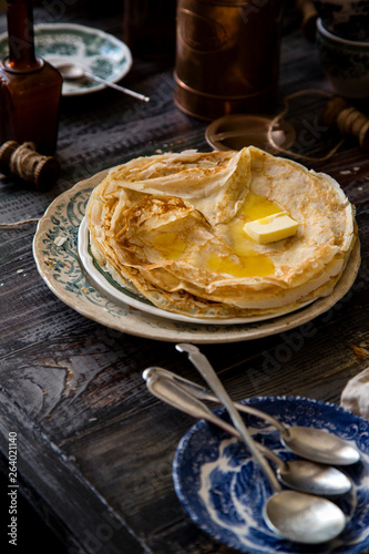 Homemade crepes with melted butter on vintage plate with green ornament stand on rustic grey table