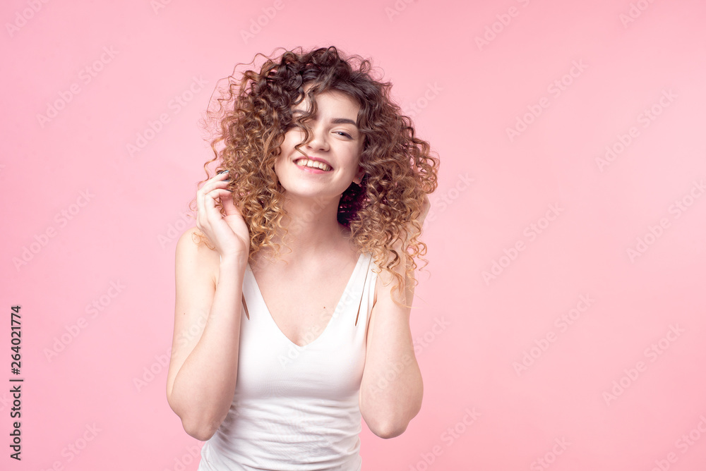 Beautiful woman with a smile on her face with amazing curls in a white T-shirt deloet laying of the hand holds accessories and styling hair curling. Beautiful woman with a smile on her face with amazing curls in a white T-shirt deloet laying of the hand holds accessories and styling hair curling.