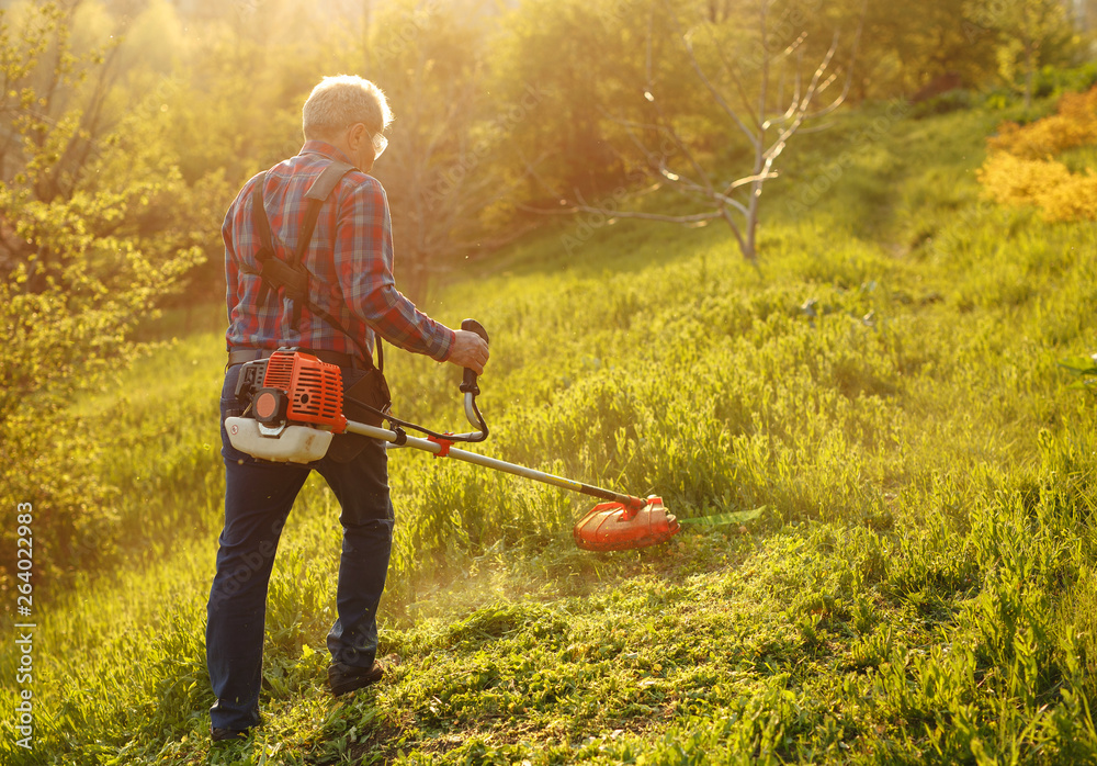 Ταπετσαρία mowing trimmer - worker cutting grass in green yard at sunset.