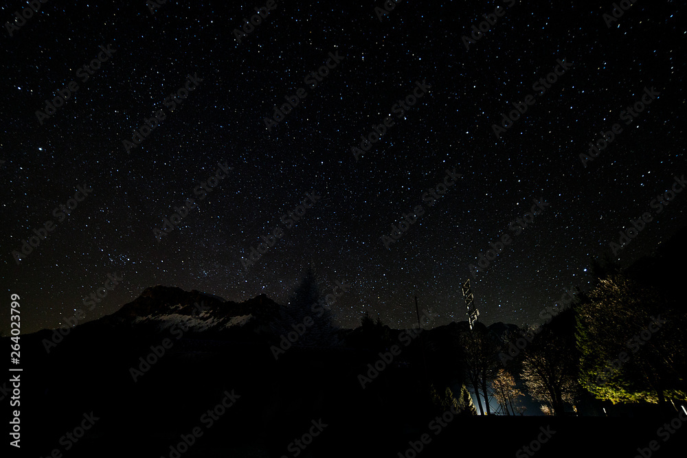 night sky star in the alps with mountains and tree silhouette in the austrian alps