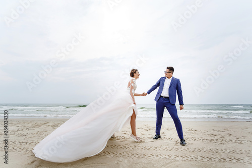 groom holds his bride tightly in a strong wind on the beach