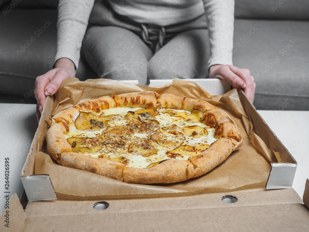 Pizza with pear and dor blue cheese in delivery box. Female hands