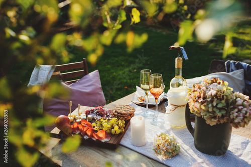summer outdoor party table with white wine, cheese and ham plate with fruits. Garden festive table.