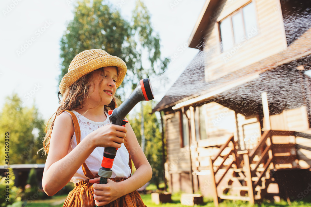 Φωτογραφία happy child girl watering flowers with hose in summer garden, holding water spri