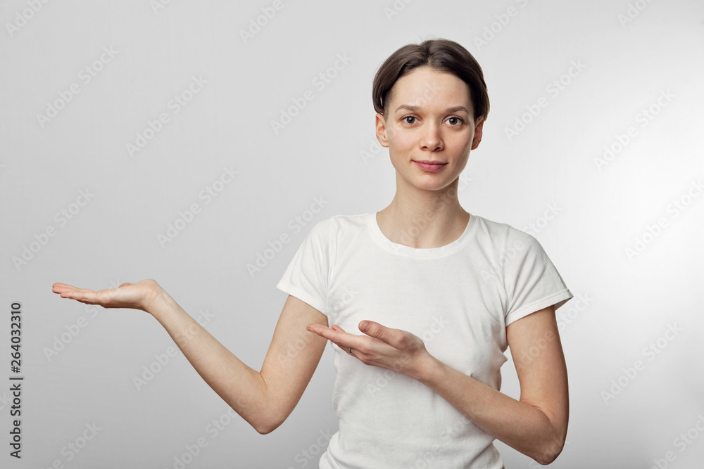 Photo of young woman standing isolated over white wall background. Looking camera showing copyspace pointing. Photo of young woman standing isolated over white wall background. Looking camera showing copyspace pointing.