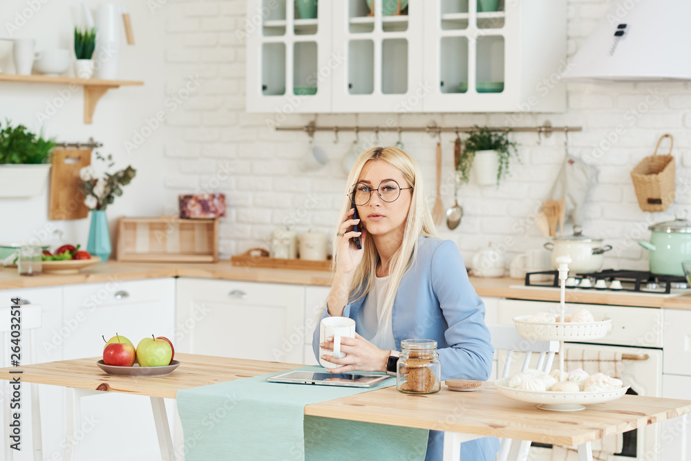 Freelance concept. Beautiful business woman in casual clothes and glasses is examining documents and smiling while working with a laptop in kitchen. Working at home Freelance concept. Beautiful business woman in casual clothes and glasses is examining documents and smiling while working with a laptop in kitchen. Working at home