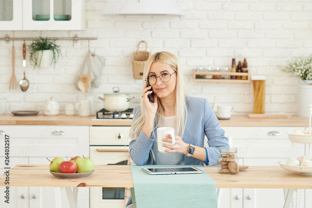 Freelance concept. Beautiful business woman in casual clothes and glasses is examining documents and smiling while working with a laptop in kitchen. Working at home Freelance concept. Beautiful business woman in casual clothes and glasses is examining documents and smiling while working with a laptop in kitchen. Working at home