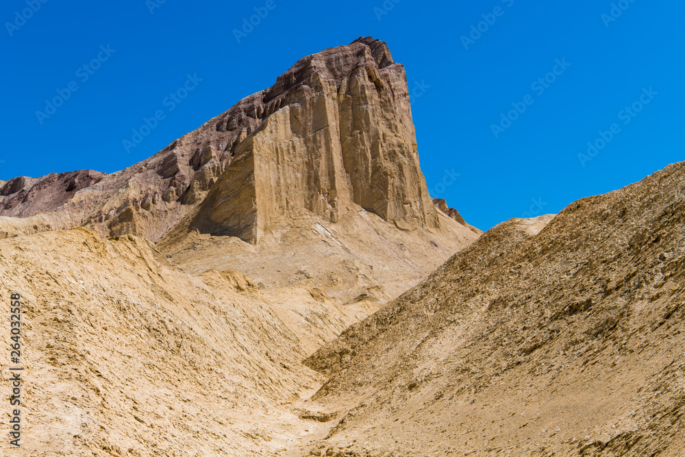 A high desert peak with sheer cliffs rises above a barren, golden desert landscape - Golden Canyon in Death Valley National Park