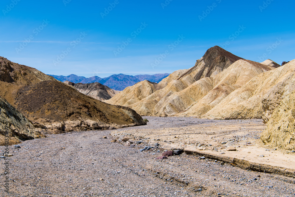 A dry rocky riverbed curves through a barren desert landscape of colorful badlands and peaks in Death Valley National Park A dry rocky riverbed curves through a barren desert landscape of colorful badlands and peaks in Death Valley National Park