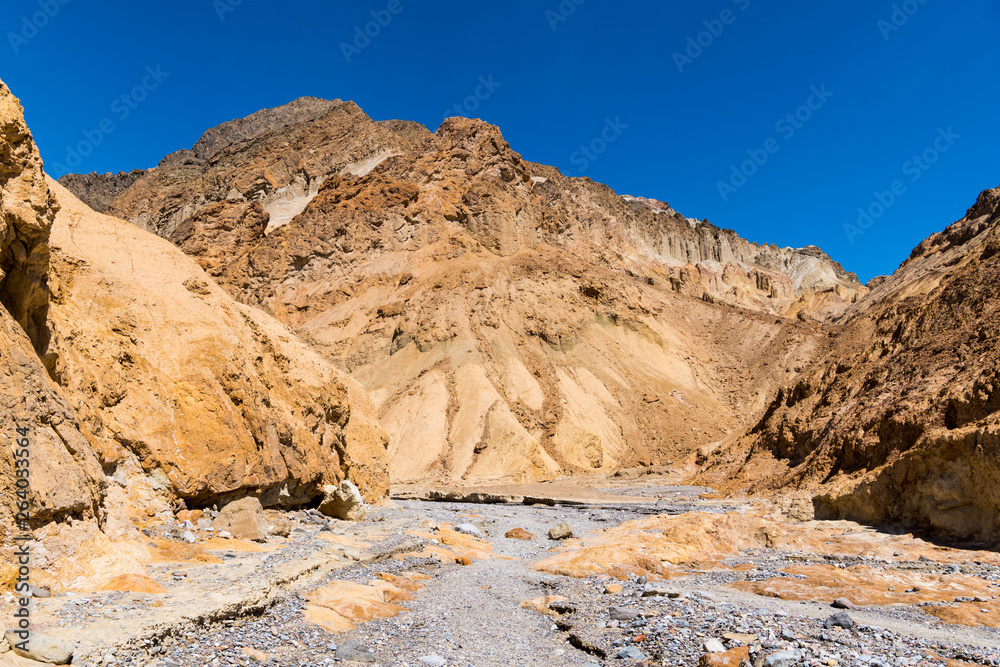 A canyon with a dry riverbed of gray rock contrasted with golden cliffs and peaks - Gower Gulch, Death Valley National Park