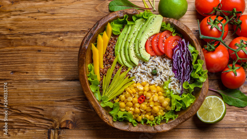 Buddha bowl with chickpea, avocado, wild rice, quinoa seeds, bell pepper, tomatoes, greens, cabbage, lettuce on old wooden table. Top view with copy space. Healthy vegan food.