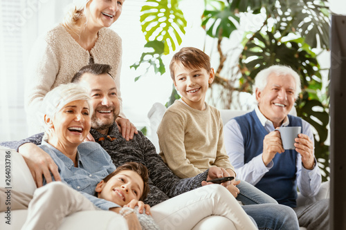 Smiling parents and kids watching television with happy grandfather