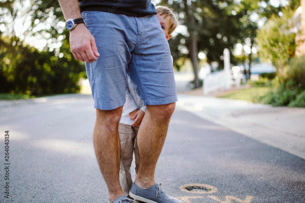 Portrait of a shy small boy peeking from behind his father's legs Portrait of a shy small boy peeking from behind his father's legs