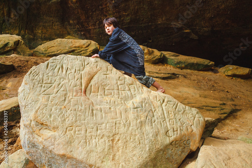 Portrait of a small barefoot boy climbing large rock in a sunlit gorge photo