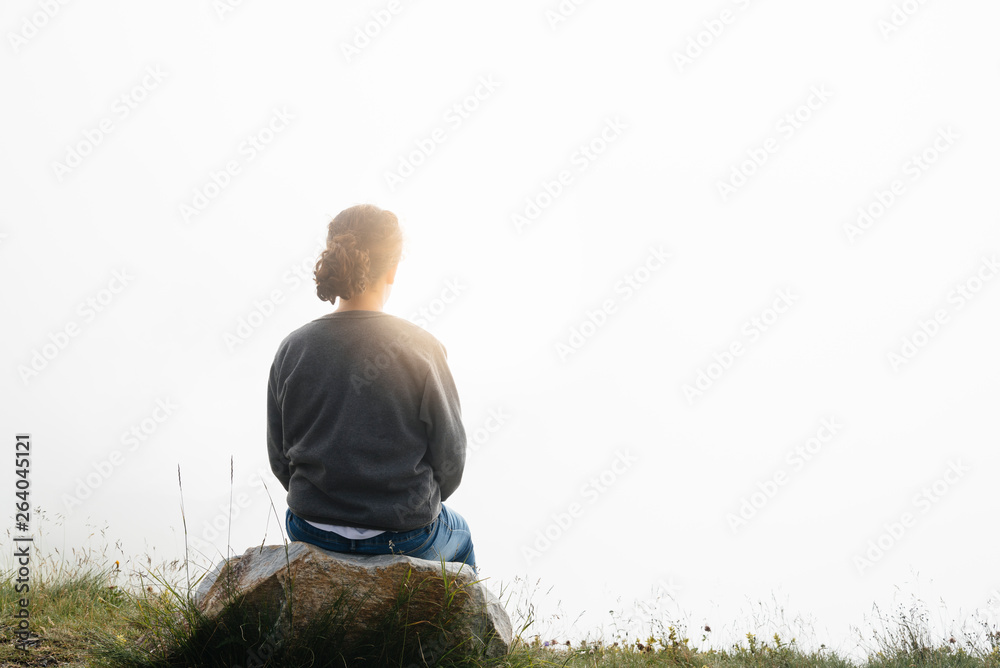 Young woman sitting against foggy landscape. Rear view Young woman sitting against foggy landscape. Rear view