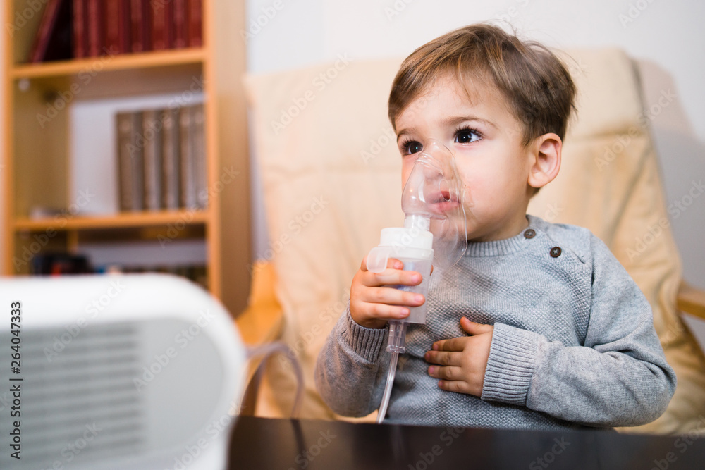 Little boy using steam inhaler nebulizer mask inhalation at home. Medical procedures vapor medication treatment asthma pneumonia bronchitis coughing Little boy using steam inhaler nebulizer mask inhalation at home. Medical procedures vapor medication treatment asthma pneumonia bronchitis coughing